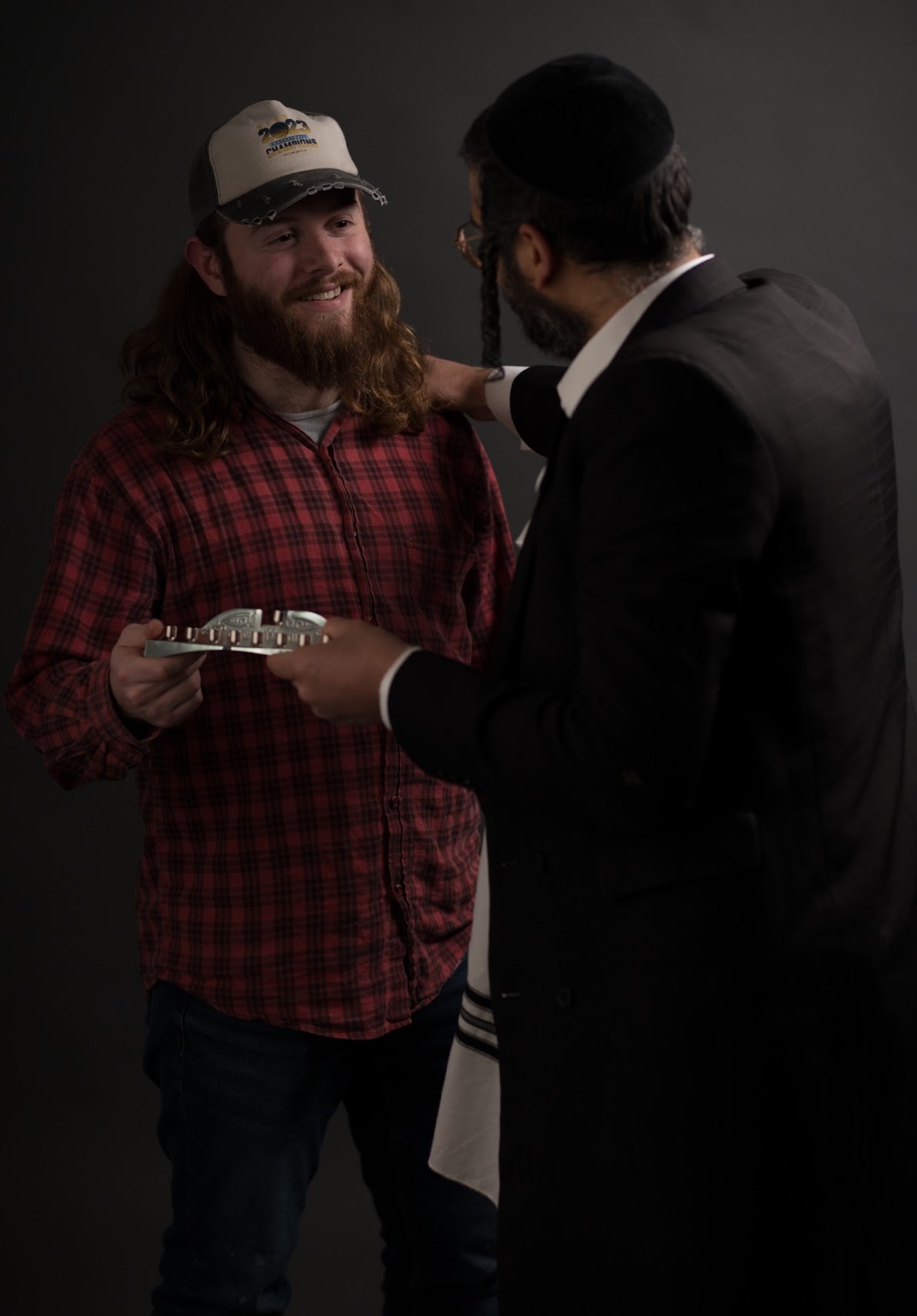 Two men sharing a menorah against a dark studio background, photographed for Yehi Ohr’s Chanukah campaign.