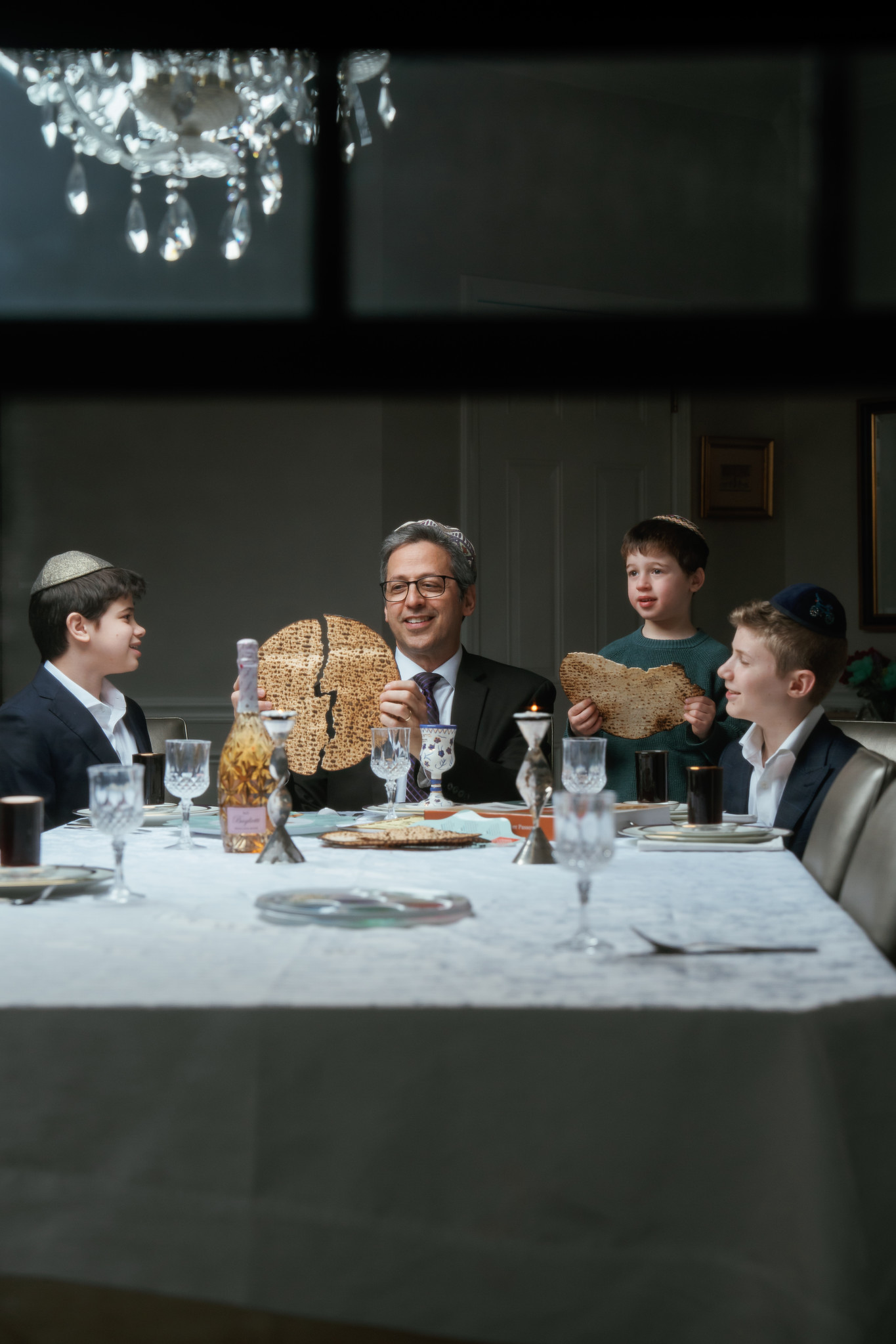 A smiling man holding matzah at a Seder table with three boys, the photograph used in Yehi Ohr’s Pesach advertisement.